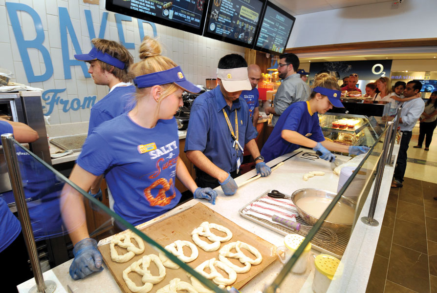 /></p>
<p></p>
<p>But while taste tests were all well and good, the Burtons had to ask some tough questions and get to the bottom of why, after five years of being in the UK, Auntie Anne’s hadn’t been able to take on more than one franchisee. “We could see that the American head-office team had struggled when it came to keeping costs down and developing a local supply chain – all the ingredients came from the US,” Burton says. “They just never grasped the opportunity.” So for the past ten years, the British master franchisees have slowly but surely been dismantling the complex supply chain, reducing costs and switching to UK suppliers. And today everything but one variety of sugar comes from Britain. “Developing a local supply chain’s been our biggest challenge,” says Burton. “It’s only really been in the last six years that we’ve had the economies of scale needed to make the changes we wanted and simplify everything.””</p>
<p></p>
<p>With these changes under way, Auntie Anne’s was growing steadily and bringing on new franchisees at an average rate of about two to four a year. Then, in 2014, Robert Burton realised the time had come for him to take a step back and hand the reins over to his son. Over the course of the following year, there was a gradual change of leadership as Max became the company’s managing director. “Taking over from my father was a bit stressful – especially since I’d just had a baby – but the actual transition itself was relatively straightforward,” Burton recalls. “We’d agreed on most things and I’d been involved in the direction of the company from the get-go so, to a large extent, it was business as usual.”</p>
<p></p>
<p>One of the first projects Burton saw through as managing director was the development of a new points-based app that allows people to clock up points digitally and redeem them in-store. “The beauty of the app is that it’s useful for our customers while helping us capture really good data about people’s purchasing habits,” Burton explains. “For example, we learned that there’s no point doing a ‘buy two get one free’ deal if our customers don’t really want three pretzels in the first place.” Since the app’s launch, Auntie Anne’s has built up a more sophisticated customer profile and is serving up tailored offers based on what people want, enabling it to win repeat business. “Customer loyalty is key and that’s what so many food businesses are chasing,” says Burton.”</p>
<p></p>
<p>The app was just one part of the franchise’s attempt to ramp up its marketing initiatives as the network grew. “Because we had such a small team at the start, we never had a marketing roadmap for how we’d develop the brand, which meant that every store had its own local plan,” says Burton. “But that’s changed.” He’s clearly making up for lost time: on top of the app-development project, Burton’s brought a marketing manager on board and the franchise is investing heavily in existing social-media platforms like Twitter and Facebook while exploring the possibility of creating a community on Snapchat and Instagram. “Investing in social media makes sense from a revenue-generating perspective but it also builds our brand profile and helps our customers get to know our personality, which is so important.””</p>
<p></p>
<p>And as Auntie Anne’s visibility in the UK increases, Burton is conscious about striking the balance between localising the brand and respecting its all-American roots. “While we don’t wave an American flag over our stores, we don’t shy away from the fact that the brand hails from the US either,” he says. So when head office developed a new product featuring chocolate-chip-studded cream cheese – which has proved popular in America – Burton deemed it unsuitable for more conservative British tastes. But at the same time, the franchise is more than happy to include American lingo in its marketing collateral. “US franchises like McDonald’s and Subway have gone down well here when introduced properly, so we by no means Anglicise our content for the UK.”</p>
<p></p>
<p>All this has helped Auntie Anne’s grow its network from just one franchisee to 31. And Burton’s not stopping there. “I want to have 40 franchisees signed up by the end of the year,” he says. “The goal is to see an Auntie Anne’s franchise in 120 locations across the country, whether they be shopping centres, train stations, airports or high streets.” And now that it’s fully embraced marketing and technology, these ambitious plans don’t seem at all out of reach.”<img decoding=